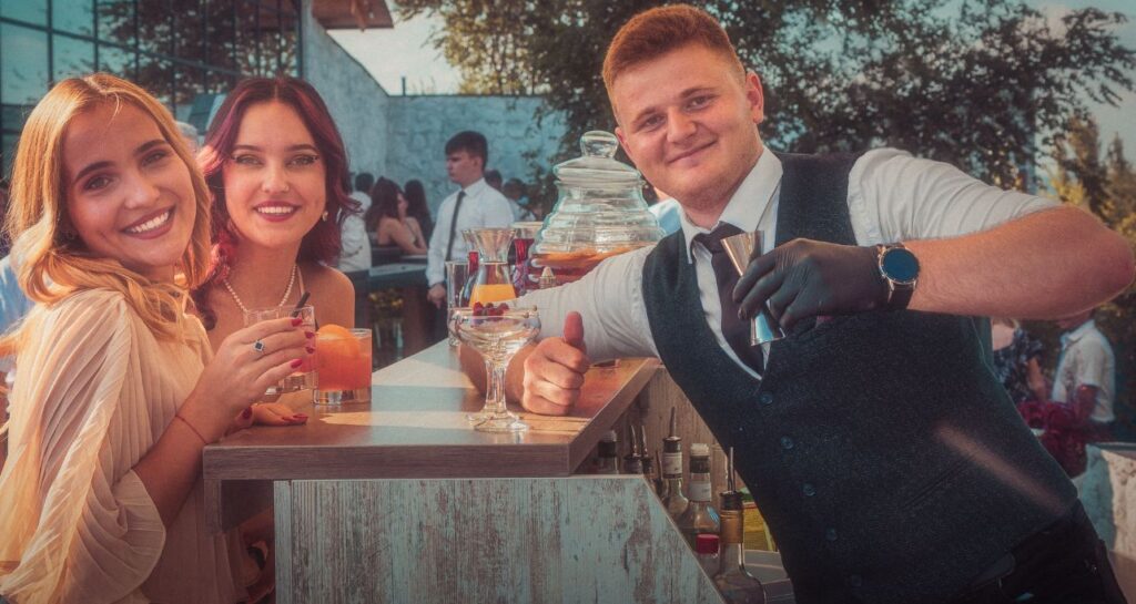 Barman la bar mobil alături de invitați cu cocktailuri, atmosferă relaxată la nuntă