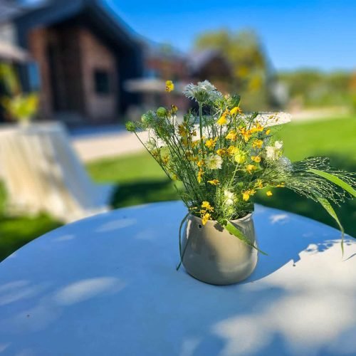 Et Cetera – cum arată o nuntă în aer liber la vinărie 4 Aranjament floral pe o masă la Et Cetera, cu clădirea vinăriei și gazonul în fundal